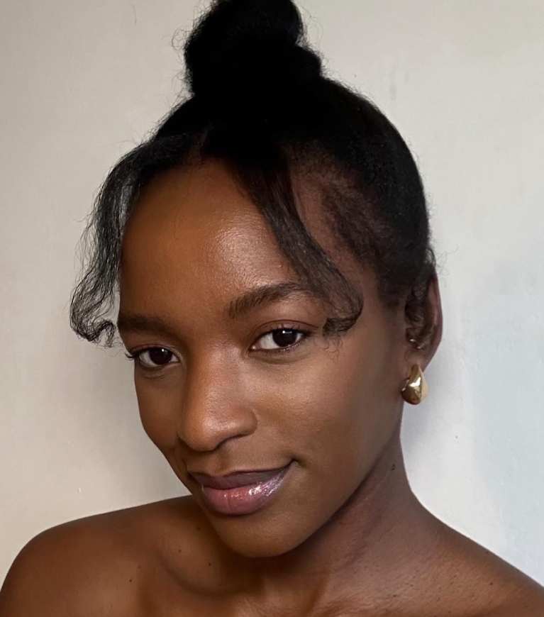 A woman smiling, with dark hair pulled into a high bun and styled baby hairs.